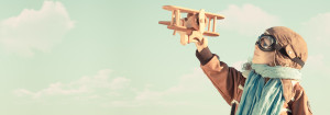 young child dressed as an old-fashioned pilot holing a wooden airplane