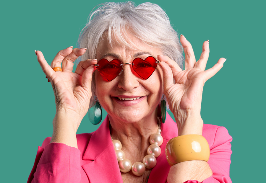 older woman smiling as she puts on heart-shaped sunglasses